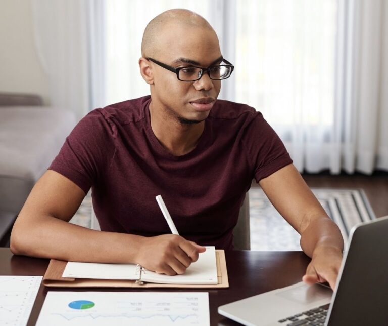 young-entrepreneur-working-from-home-reading-document-laptop-taking-notes-planner