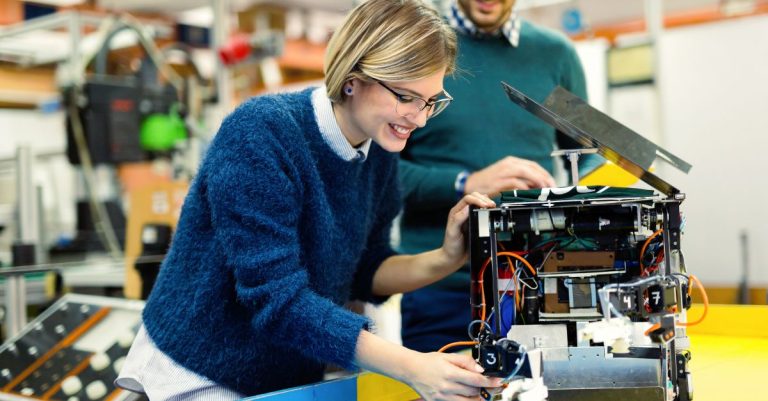 Portrait of a woman and a man looking at a robot prototype in the classroom.