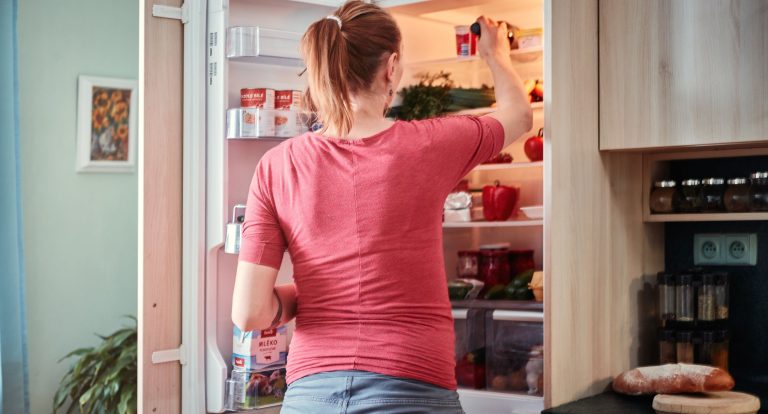 Portrait of a woman putting food in the fridge.
